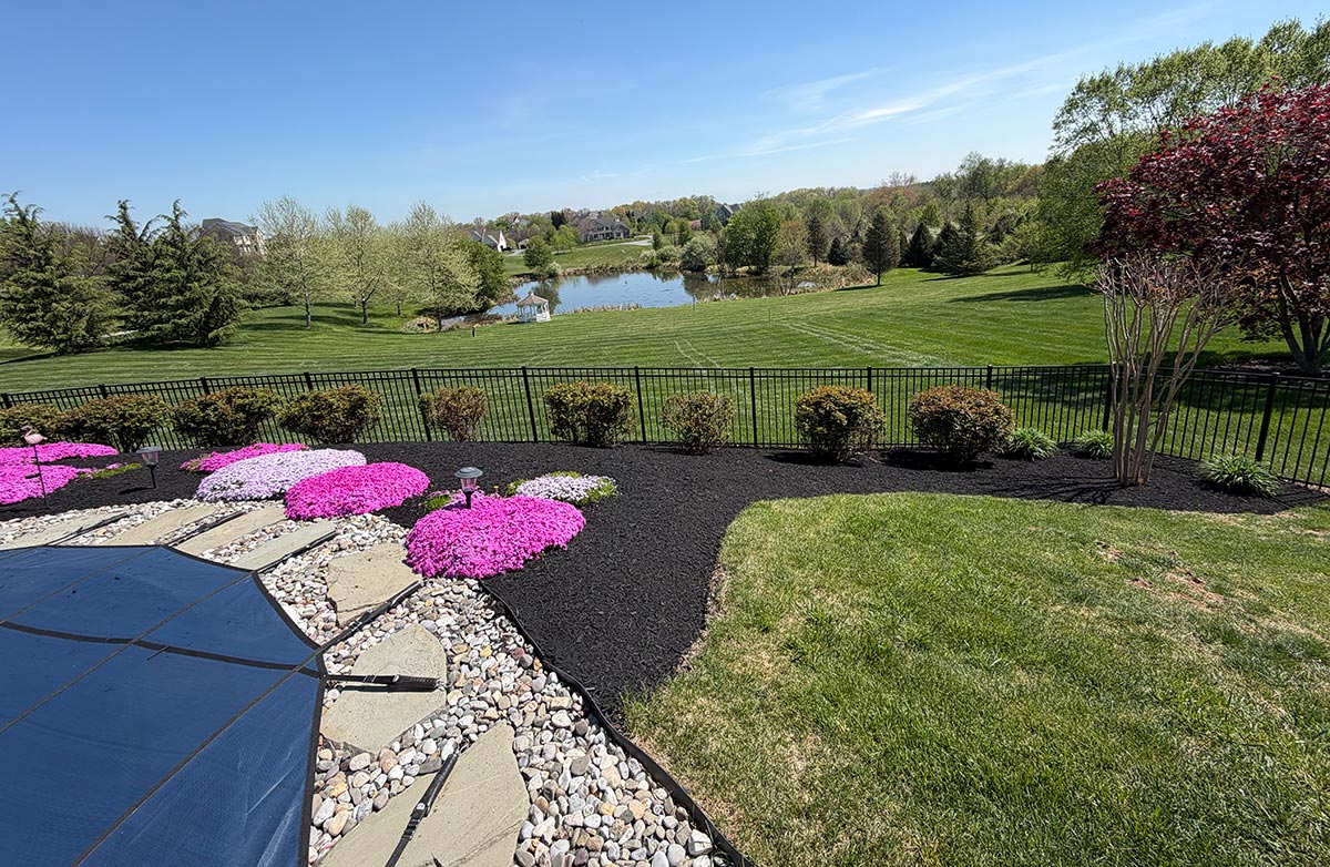 Mulched flower beds with pink phlox overlooking a backyard pond