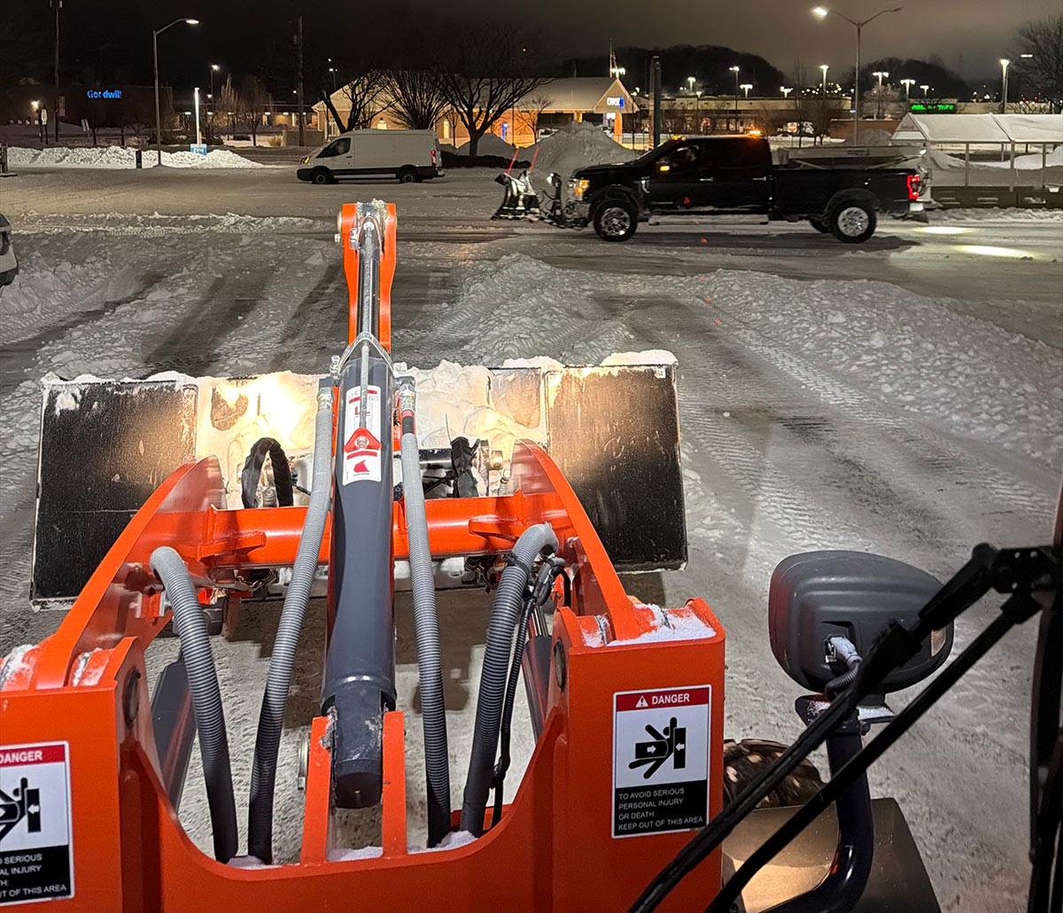 Snow plow attachment clearing a commercial lot at night